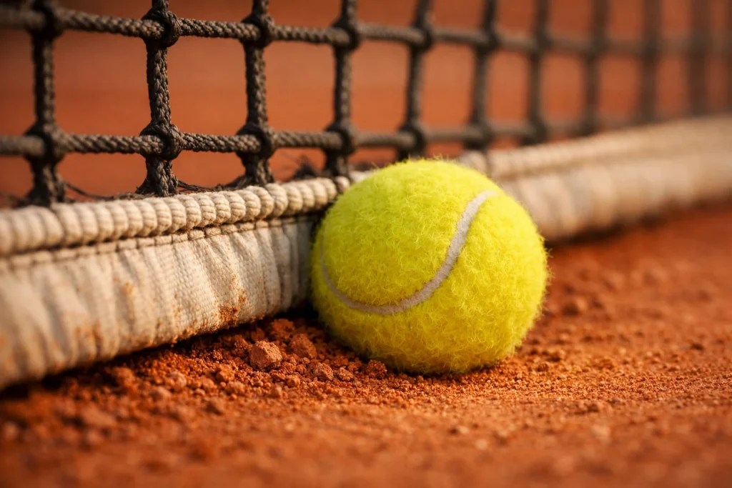 Pallina da tennis ferma contro la rete su un campo in terra battuta dopo un colpo sbagliato